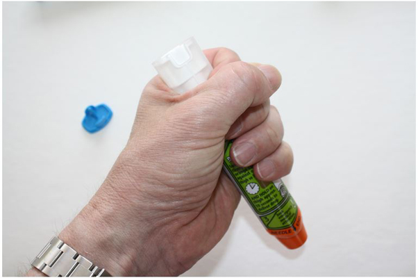 Hand making a fist around EpiPen with needle facing downward